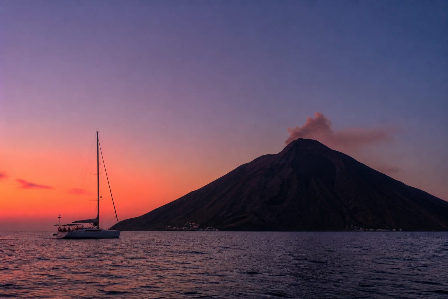 Voilier devant le Stromboli au crépuscule, fumée au sommet